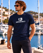 Hombre con camiseta azul marino de IMPARABL3, corte regular, manga corta y logotipo I3 blanco centrado en el pecho, junto a un puerto deportivo.