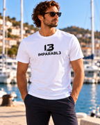 Hombre con camiseta blanca de IMPARABL3, corte regular, manga corta y logotipo I3 negro centrado en el pecho, junto a un puerto deportivo.