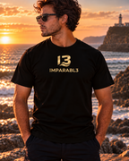 Modelo con camiseta negra de hombre Sport Style de IMPARABL3, vista frontal con logotipo dorado en el pecho, junto al mar al atardecer.