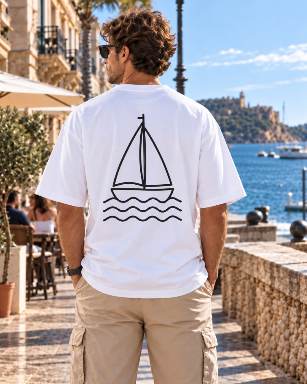 Hombre con camiseta oversize blanca de IMPARABL3 vista de espalda con diseño de velero y olas