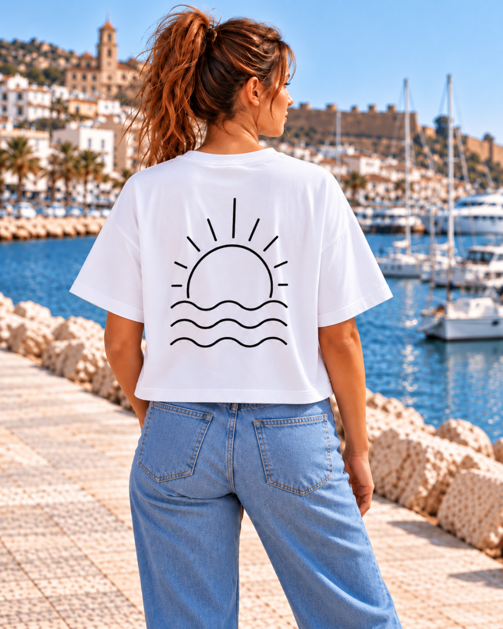 Vista trasera de la camiseta oversize blanca de mujer de IMPARABL3, con ilustración negra de un sol naciente sobre tres olas y corte holgado de talle corto.