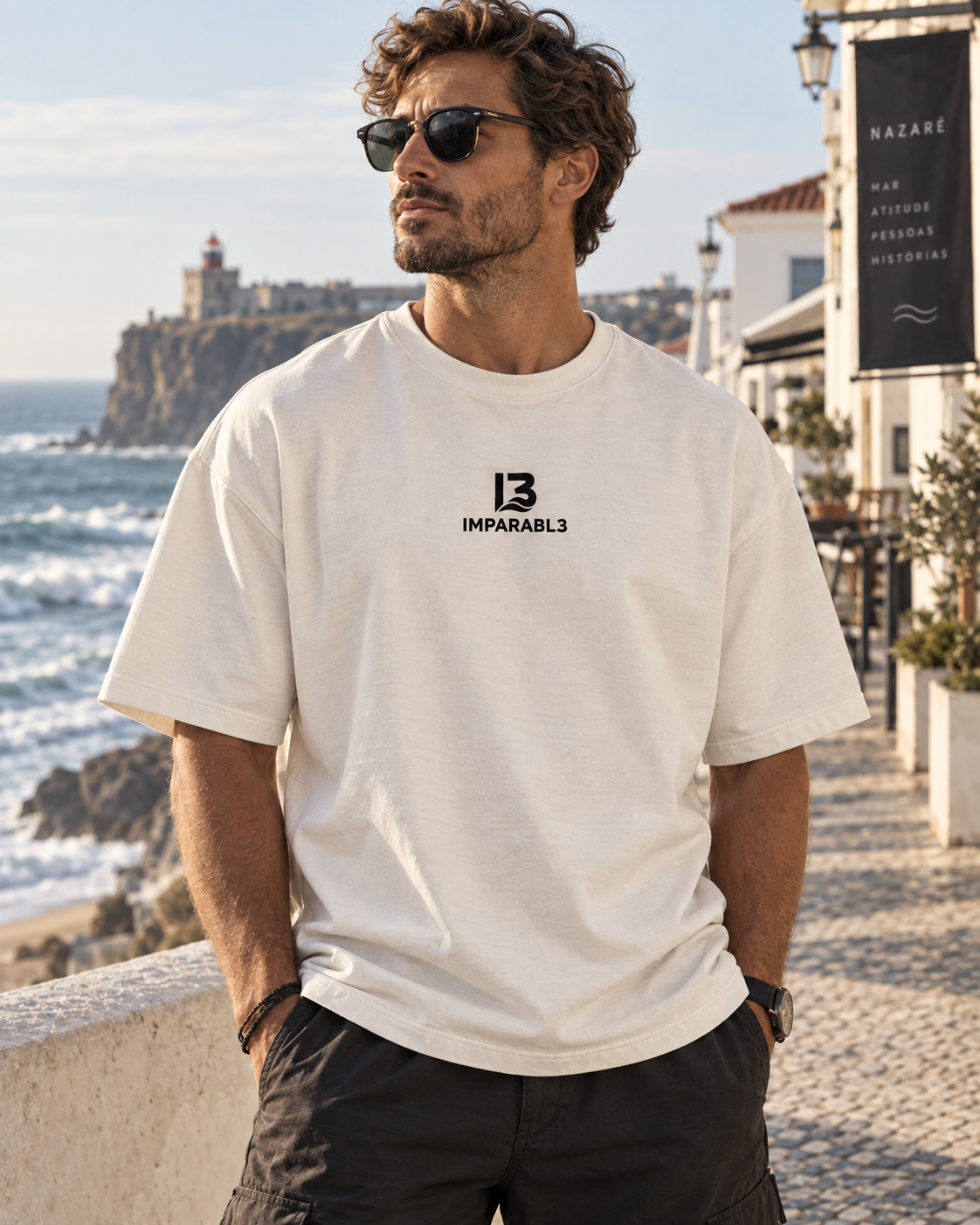 Modelo masculino con camiseta oversize de IMPARABL3 en blanco vintage, mostrando el logo frontal en un entorno costero