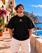 Camiseta oversize negra para hombre de IMPARABL3, vista frontal con logotipo I3 blanco en el pecho, presentada por modelo en entorno costero mediterráneo.