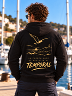 Sudadera negra de hombre Sport Style de IMPARABL3, vista trasera con capucha, ilustración dorada de gaviota, mar y faro y la frase «La fuerza nace de resistir al temporal».