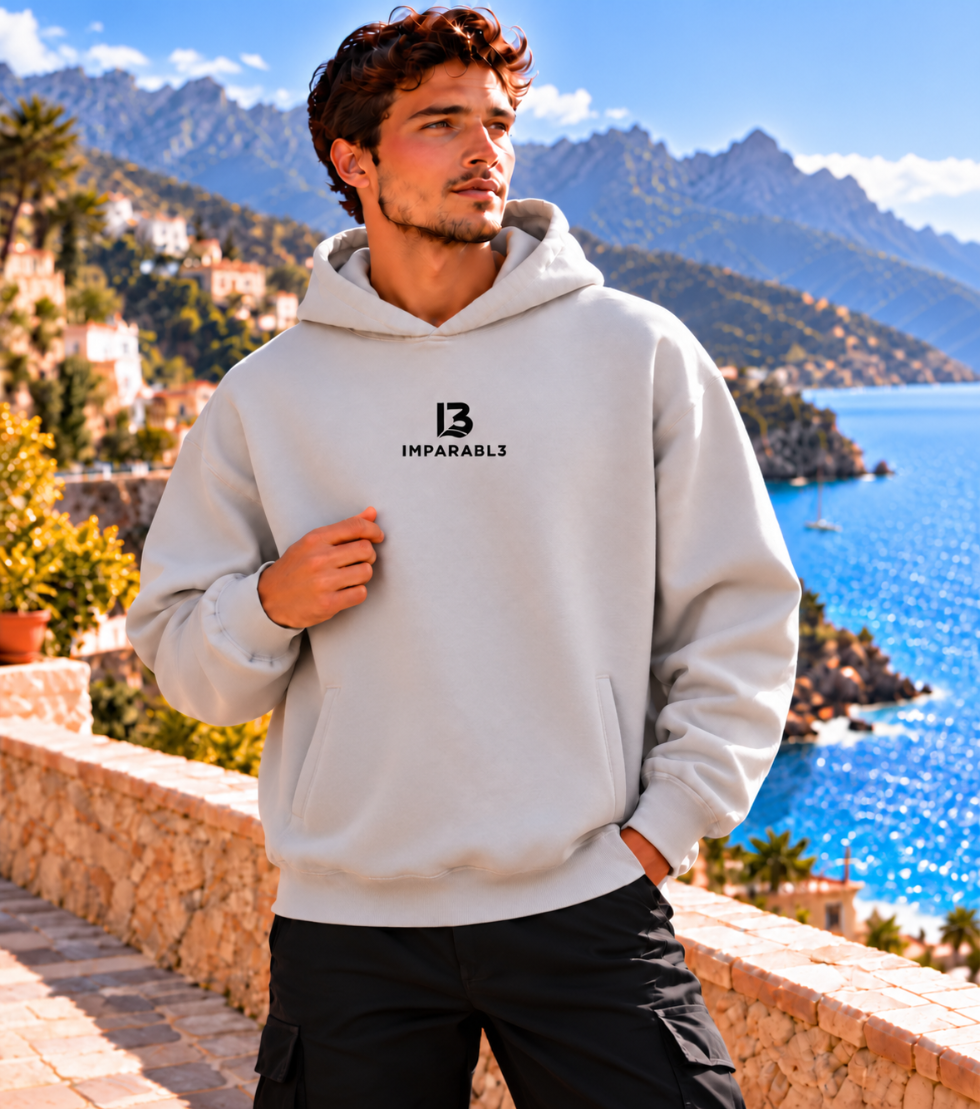 Hombre con sudadera oversize gris piedra de IMPARABL3, vista frontal, logotipo I3 negro centrado en el pecho y bolsillo tipo canguro.